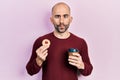 Young bald man drinking coffee and eating pastry making fish face with mouth and squinting eyes, crazy and comical Royalty Free Stock Photo