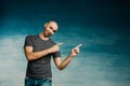 A young bald man in a gray T-shirt on a blue background fooling around and points to the side