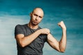 Young bald man in a gray T-shirt and jeans boasts of his biceps Royalty Free Stock Photo