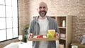 Young bald man holding breakfast tray standing at bedroom Royalty Free Stock Photo