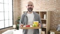 Young bald man holding breakfast tray standing at bedroom Royalty Free Stock Photo
