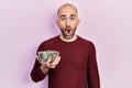 Young bald man holding sunflower seeds bowl scared and amazed with open mouth for surprise, disbelief face Royalty Free Stock Photo