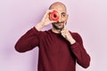 Young bald man holding tasty colorful doughnut on eye serious face thinking about question with hand on chin, thoughtful about Royalty Free Stock Photo
