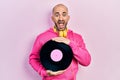 Young bald man holding vinyl disc celebrating crazy and amazed for success with open eyes screaming excited