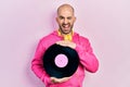 Young bald man holding vinyl disc winking looking at the camera with sexy expression, cheerful and happy face Royalty Free Stock Photo