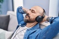 Young bald man listening to music relaxed on sofa at home