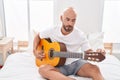 Young bald man playing classical guitar sitting on bed at bedroom Royalty Free Stock Photo
