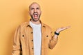 Young bald man presenting with open palms, holding something angry and mad screaming frustrated and furious, shouting with anger