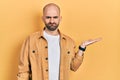 Young bald man presenting with open palms, holding something skeptic and nervous, frowning upset because of problem Royalty Free Stock Photo