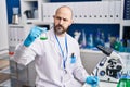 Young bald man scientist holding test tube writing on notebook at laboratory Royalty Free Stock Photo