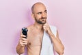 Young bald man shirtless holding electric razor serious face thinking about question with hand on chin, thoughtful about confusing Royalty Free Stock Photo