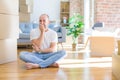 Young bald man sitting on the floor around cardboard boxes moving to a new home looking stressed and nervous with hands on mouth