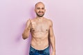 Young bald man standing shirtless doing happy thumbs up gesture with hand Royalty Free Stock Photo
