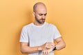 Young bald man wearing casual white t shirt checking the time on wrist watch, relaxed and confident