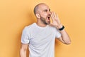 Young bald man wearing casual white t shirt shouting and screaming loud to side with hand on mouth