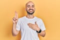 Young bald man wearing casual white t shirt smiling swearing with hand on chest and fingers up, making a loyalty promise oath Royalty Free Stock Photo