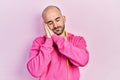 Young bald man wearing gym clothes and using headphones sleeping tired dreaming and posing with hands together while smiling with Royalty Free Stock Photo