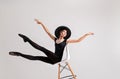 Young ballerina in black pointe shoes and an elegant hat flies along with chair on gray background Royalty Free Stock Photo