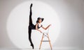 Young ballerina in black pointe shoes and an elegant hat flies along with chair on gray background Royalty Free Stock Photo