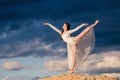 Young ballerina in a light long white dress stands in an arabesque