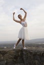 Young ballerina in white dress and satin ballet shoes posing on the edge of old fortress wall on a grey sky background Royalty Free Stock Photo