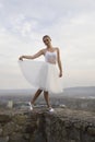 Young ballerina in white dress and satin ballet shoes posing on the edge of old fortress wall on a grey sky background Royalty Free Stock Photo