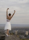 Young ballerina in white dress and satin ballet shoes posing on the edge of old fortress wall on a grey sky background Royalty Free Stock Photo