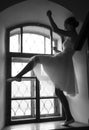 Young ballerina in white dress and satin ballet shoes posing on a old window in a dark room. black and white Royalty Free Stock Photo