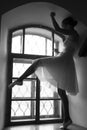 Young ballerina in white dress and satin ballet shoes posing on a old window in a dark room. black and white Royalty Free Stock Photo