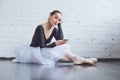 Young ballet dancer sitting leaning white wall using phone in studio active lifestyle