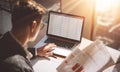 Young banking finance analyst in eyeglasses working at sunny office on laptop while sitting at wooden table.Businessman Royalty Free Stock Photo