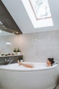 Young bare woman laying in white bubble bathtub with raised leg.