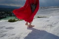 Young barefoot girl in red dress walk on white travertines in Pamukkale