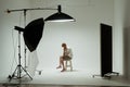 Young barefoot man sits on chair in pose of thinker posing in photo studio. Male model wearing white shirt on white
