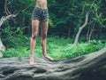 Young barefoot woman standing on fallen tree in forest