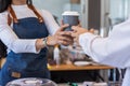 Young barista delivers hot coffee in take away paper cup to customer before making payment at counter. cashier is delivering hot