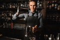 Young barman pouring a clear alcoholic drink on the bar counter