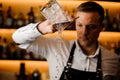 Young barman pouring water from a glass with ice cubes