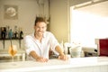 Young barman smiling in beach bar with cocktail and bottles in a sunny day Royalty Free Stock Photo