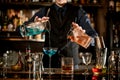 Young bartender professionally pours cocktails into glasses.