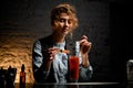 Young bartender woman mixes by spoon glass with bloody mary cocktail.
