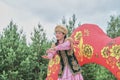 Young Bashkir woman in folklore clothes performing traditional dance on stage while rural holiday