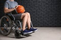 Young basketball player sitting in wheelchair against dark brick wall Royalty Free Stock Photo