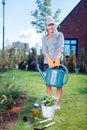 Young beaming gardener wearing comfortable clothes holding garden sprinkler