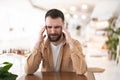 Young bearded attractive man suffering extreme headache during his lunch break in the cafe, healthcare and medicine context