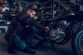 Young Bearded Biker Tuning Motorcycle in Garage.