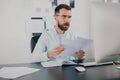 Young bearded brunette man looking amazed while working on business project in his modern office, holding documents in Royalty Free Stock Photo