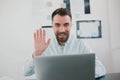 Young bearded brunette man looking friendly waving his friend during online skype conversation at workplace , communication Royalty Free Stock Photo