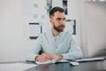 Young bearded brunette man sits in his office looking happy while working on business project looks satisfied, takes Royalty Free Stock Photo
