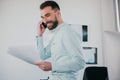 Young bearded brunette man working on business project in his modern office, holding documents in one hand and smartphone in other Royalty Free Stock Photo